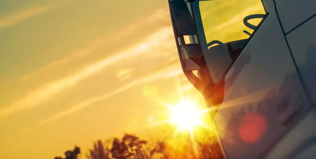 Primo piano della cabina di un camion illuminato dalla luce del tramonto, con il sole basso all'orizzonte e riflessi dorati sulla carrozzeria.