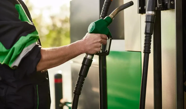 Primo piano di un addetto al rifornimento carburante che impugna una pompa verde presso una stazione di servizio.