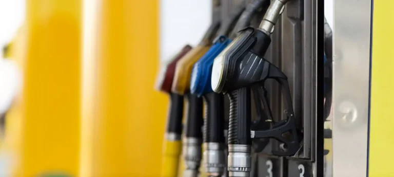 Primo piano di pompe di carburante di diversi colori agganciate a una colonnina di rifornimento presso una stazione di servizio.